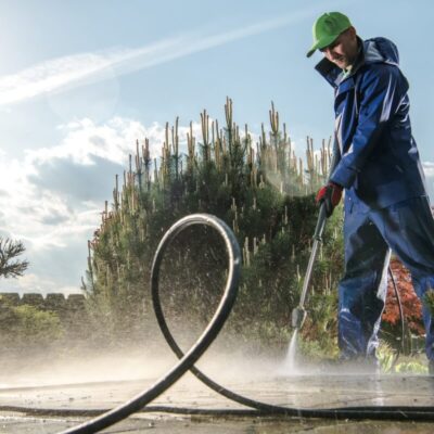 Mężczyzna w niebieskim kombinezonie wykonujący mycie dachów za pomocą myjki ciśnieniowej.