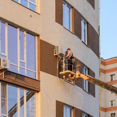 Pracownik na podnośniku wykonuje mycie wysokociśnieniowe fasady budynku.