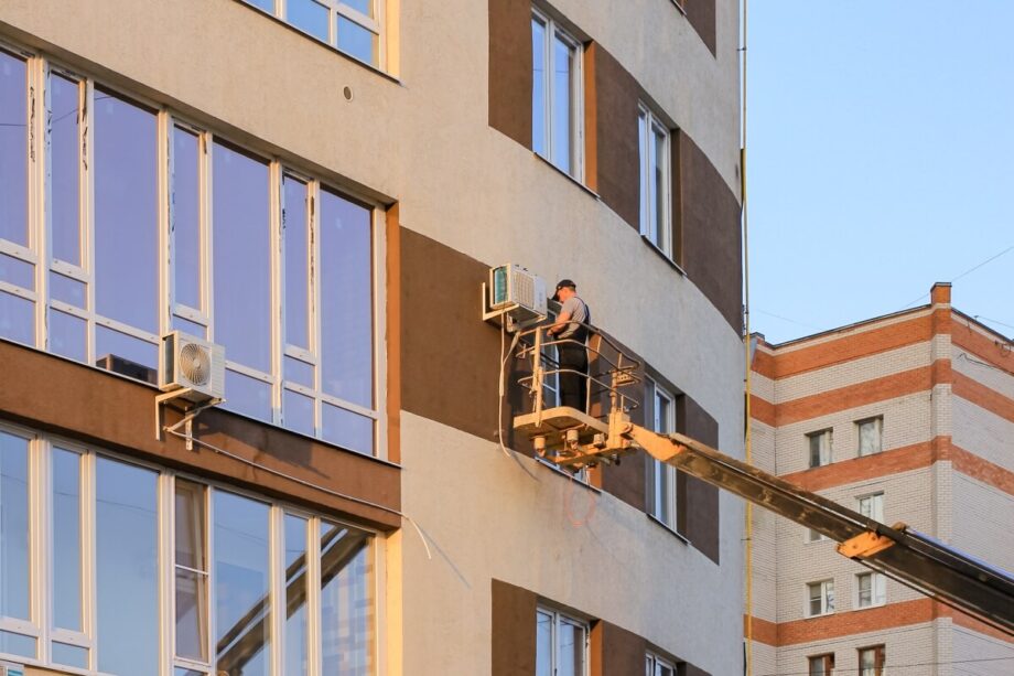 Pracownik na podnośniku wykonuje mycie wysokociśnieniowe fasady budynku.