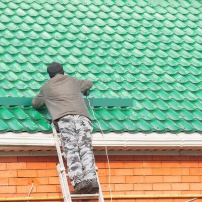 Mężczyzna na drabinie zajmuje się malowaniem dachów na zielono.