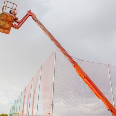Osoba na podnośniku wykonuje prace wysokościowe przy siatce.