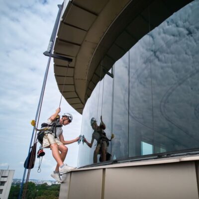 Osoba wykonuje prace wysokościowe, czyszcząc okna na dużej wysokości.