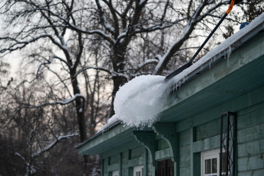 Osoba odśnieża dachy, usuwając śnieg z budynku.