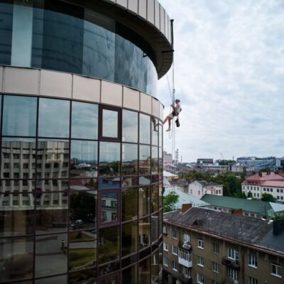 Mężczyzna zawieszony na linach wykonuje mycie elewacji szklanego budynku.